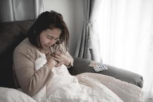 une femme malade asiatique s'assoit sur le canapé reste à la maison, la femme se sentait mal, voulait s'allonger et se reposer, forte fièvre photo