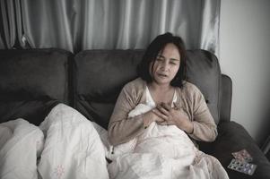 une femme malade asiatique s'assoit sur le canapé reste à la maison, la femme se sentait mal, voulait s'allonger et se reposer, forte fièvre photo