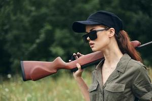 femme sur Extérieur avec une pistolet sur sa épaule dans des lunettes de soleil est en marchant le chasser photo