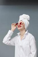 portrait de une femme rouge des lunettes de soleil produits de beauté avec serviette sur tête isolé Contexte photo