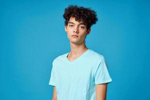 gars avec frisé cheveux dans bleu T-shirt tondu vue studio photo