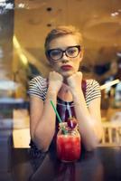 une femme avec une court coiffure est assis dans une café seul avec une cocktail photo