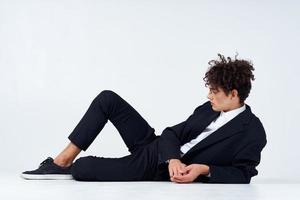 une gars une adolescent dans une costume mensonges sur le sol et baskets frisé cheveux lumière Contexte photo