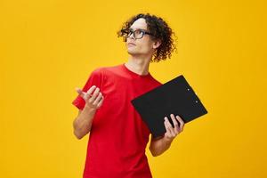 pensif myope Jeune étudiant homme dans rouge T-shirt marrant lunettes détient tablette dossier avec étude Remarques point main de côté posant isolé sur Jaune Contexte. gratuit endroit pour publicité. éducation Université concept photo