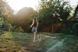 une femme court sa retour à le caméra avec une chien dans le forêt pendant un soir marcher dans le forêt à le coucher du soleil dans l'automne. mode de vie des sports formation avec votre bien-aimée chien photo