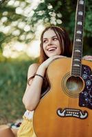 Jeune hippie femme avec éco image souriant et à la recherche dans le caméra avec guitare dans main dans la nature sur une voyage photo