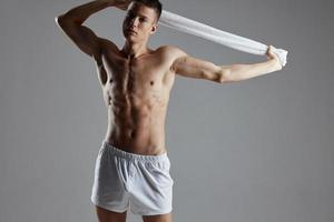gars avec une nu torse en portant une serviette dans le sien mains blanc short faire des exercices motivation isolé Contexte photo