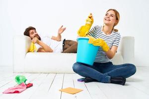 femme avec une seau dans caoutchouc gants à Accueil mari mensonges sur le canapé nettoyage photo