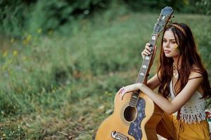 content hippie femme avec une guitare relaxant dans la nature séance sur une plaid souriant et profiter le voir. mode de vie dans harmonie avec la nature et soi photo