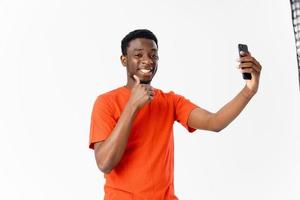 content gars de africain apparence dans un Orange T-shirt avec une mobile téléphone sur une lumière Contexte photo