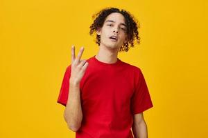 mignonne marrant caucasien Jeune homme dans rouge T-shirt spectacle signe v geste posant isolé sur plus de Jaune studio Contexte. le meilleur offre avec gratuit endroit pour publicité. émotions pour tous les jours concept photo