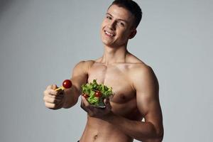 de bonne humeur sportif gars avec une nu torse assiette avec salade en bonne santé nourriture énergie photo