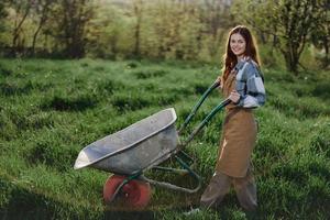 une content femme avec une Chariot travaux dans sa pays Accueil dans le campagne contre une toile de fond de vert herbe et le coucher du soleil Soleil photo