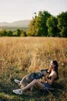 femme séance dans champ avec teckel chien souriant tandis que dépenses temps dans la nature avec ami chien dans l'automne à le coucher du soleil tandis que en voyageant photo