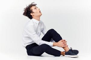 une adolescent dans une costume et baskets est assis sur le sol dans une brillant pièce côté vue photo