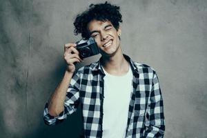 photographe dans une plaid chemise avec une caméra dans le sien main sur une gris Contexte dans une loisir studio pièce photo