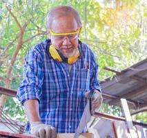 Artisan charpentier asiatique âgé utilise des scies circulaires pour traiter le bois pour les meubles photo