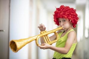 une enfant dans une brillant perruque pièces le trompette. marrant garçon avec une jouet musical instrument. futur artiste photo