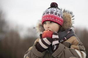 enfant dans le hiver avec fruit. garçon en mangeant une rouge Pomme photo