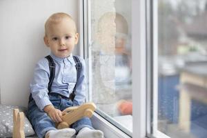 peu bébé près le la fenêtre. le enfant avec une jouet est assis sur une fenêtre seuil.deux année vieux enfant photo