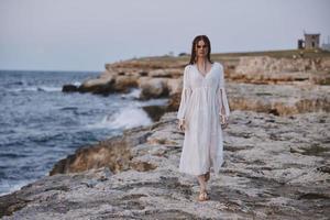 jolie femme dans blanc robe en marchant sur le rochers océan photo