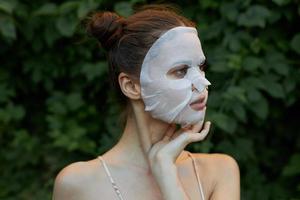 agréable fille cosmétique masque détient le sien main près le sien visage et regards une façon nu épaules feuilles dans le Contexte photo