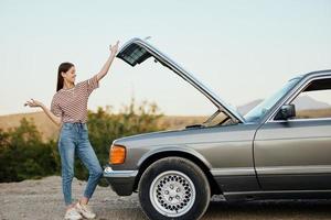 une femme des stands à l'extérieur une en panne, dangereux vieux voiture avec une clé sur le route en voyageant seul photo