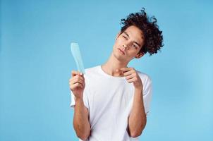 émotif homme avec une peigne dans le sien main et frisé cheveux dans une bleu Contexte copie espace photo