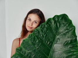 femme dans une rouge T-shirt détient une vert feuille dans sa main nettoyer peau et photo