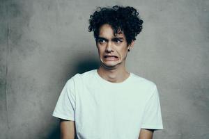 gars avec frisé cheveux dans une blanc T-shirt est assis sur chaises studio photo