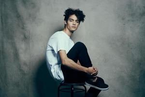 mignonne gars avec frisé cheveux séance sur une chaise studio photo