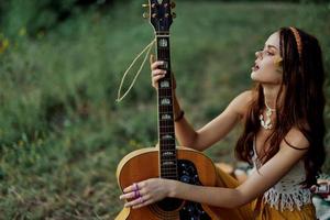hippie éco amical femme avec une guitare relaxant dans la nature séance sur une plaid par le Lac dans le soir dans le des rayons de le réglage Soleil. une mode de vie dans harmonie avec le corps et la nature photo