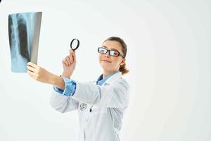 une infirmière dans une blanc manteau regards à un radiographie par une grossissant verre photo