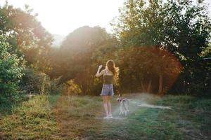 une femme court sa retour à le caméra avec une chien dans le forêt pendant un soir marcher dans le forêt à le coucher du soleil dans l'automne. mode de vie des sports formation avec votre bien-aimée chien photo