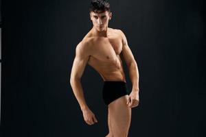 attrayant Masculin bodybuilder avec musclé corps posant foncé Contexte photo