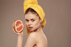 jolie femme avec serviette sur sa tête nettoyer peau à nu épaules agrumes fruit dans mains photo