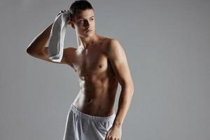 athlétique homme dans blanc short serviette dans mains posant gonflé torse isolé Contexte photo