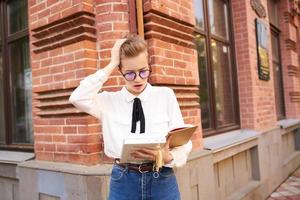 jolie femme avec des lunettes en marchant autour le ville avec une livre éducation photo