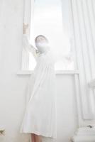 jolie femme dans blanc robe des stands près de le Soleil luxe photo