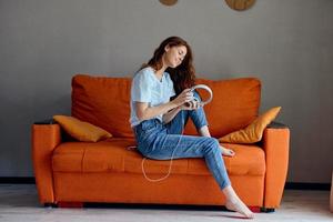 de bonne humeur femme sur le Orange canapé écoute à la musique avec écouteurs mode de vie photo