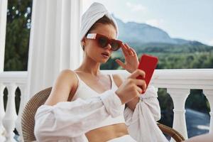 portrait de Jeune femme avec une rouge mobile téléphone séance sur le balcon paresseux Matin photo
