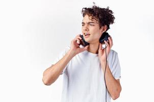 émotif gars avec frisé cheveux dans écouteurs écoute à la musique sur une lumière Contexte photo