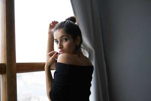 brunette dans une noir robe près le fenêtre posant élégant style photo
