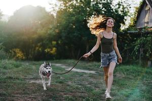 femme et sa rauque chien Heureusement fonctionnement par le herbe dans la nature dans le parc sourire avec les dents tomber marcher avec animal de compagnie, en voyageant avec une chien ami photo