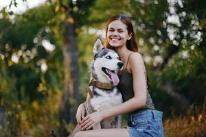 joyeux femme avec une rauque race chien souriant tandis que séance dans la nature sur une marcher avec une chien sur une laisse l'automne paysage sur le Contexte photo