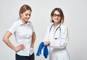 femme médecin dans une médical robe et dans bleu gants avec une stéthoscope autour sa cou et une femelle patient photo