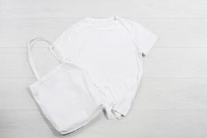 maquette T-shirt blanc client Sac à main sur bois Contexte. Haut vue copie espace achats éco réutilisable sac. modèle Vide coton Matériel Toile T-shirt chiffon. vide maquette chemise plage en tissu photo