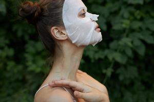 agréable femme anti-rides masque côté vue de émouvant avec mains près le cou nu épaules photo