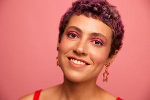 mode portrait de une femme avec une court la Coupe de cheveux de violet Couleur et une sourire avec les dents dans une rouge Haut sur une rose Contexte bonheur photo