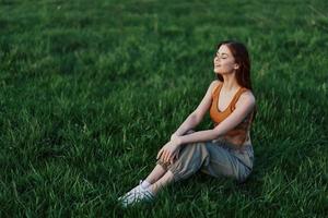 une content femme regards en dehors à le réglage été Soleil séance sur le Frais vert herbe dans le parc et souriant, vue de au-dessus de. le concept de soins auto-administrés photo